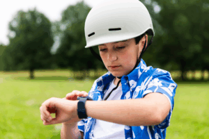A child wearing a bike helmet outdoors checking his kids GPS smart watch.